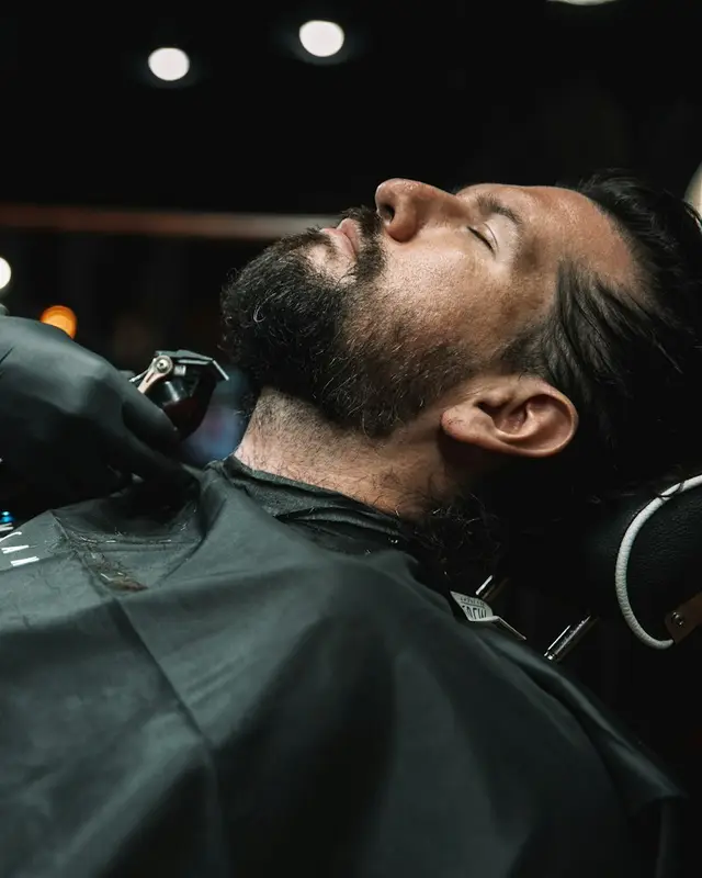 Barbeiro aparando a barba de um cliente deitado na cadeira